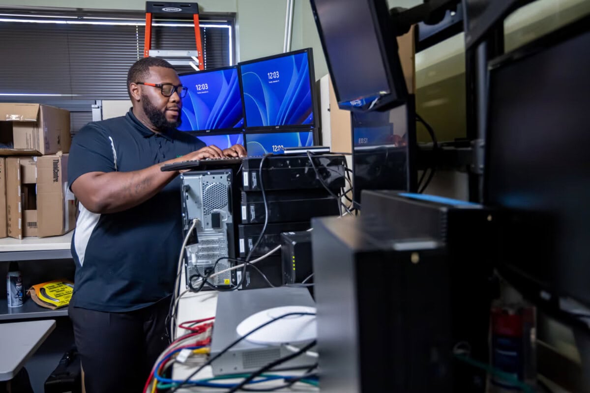 IT technician working on a computer server with multiple monitors in a tech workspace.